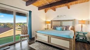 A bedroom with a large window, a bed with a blue bedspread, two bedside lamps, and a chair. - Highland Park Panorama by Avantstay Game Room + Panoramic Views Wine Country (Paso Robles)