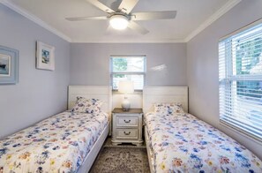 A bedroom with two single beds, a ceiling fan, a window with blinds, and a small bedside table with a lamp. - Sunny Boynton Oasis: Pool, Tiki Hut & Paradise! (Boynton Beach)