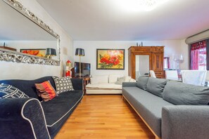A living room with a dark sofa, a grey sofa, a flat-screen TV, a painting, and a wooden cabinet. - Schiaccianoci Apartment (Rome)