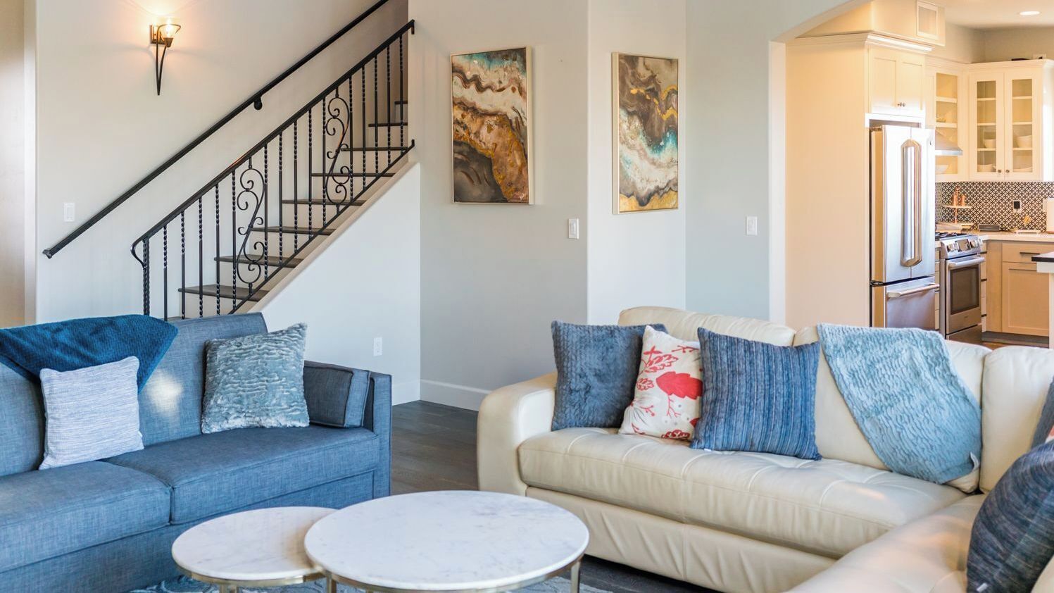 A living room with two sofas, a coffee table, a staircase, and a kitchen area with cabinets and appliances.