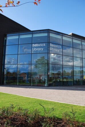 A modern glass building with 'Beswick Library' signage, surrounded by a paved area and greenery. - Stylish 3-Bed Home | Free Parking | Near Etihad Stadium & Co-op Live Arena (Manchester)