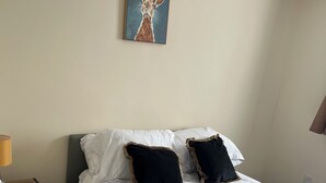 Ein Hotelzimmer mit Bett, Kissen, Nachttisch, Lampe und einem Bild an der Wand.