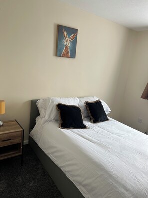 Ett hotellrum med en säng, kuddar, ett nattduksbord, en lampa och en tavla på väggen.