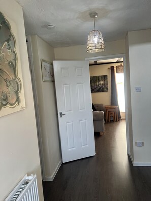 Un couloir avec une porte blanche, un radiateur, un luminaire au plafond et un tableau accroché au mur.
