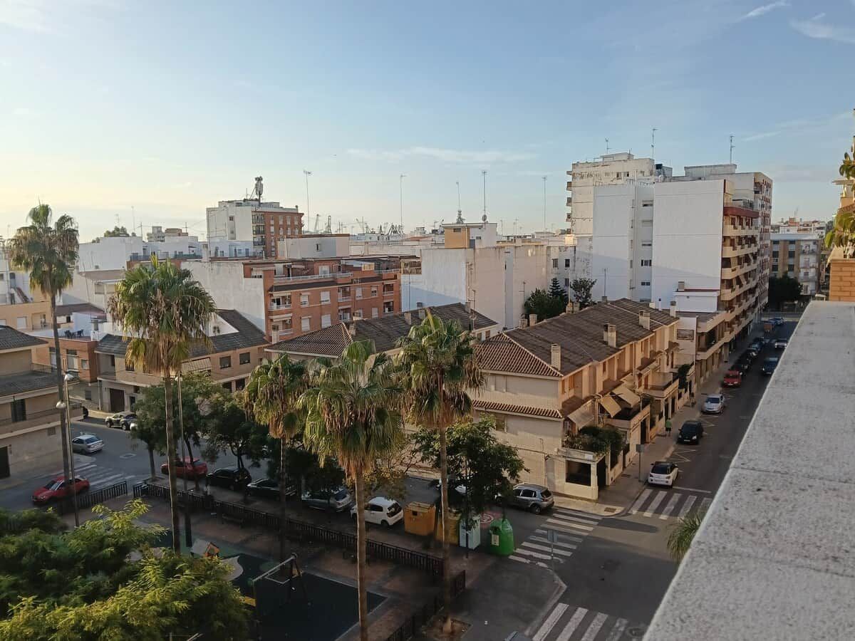 A cityscape with buildings, palm trees, and a street with parked cars.