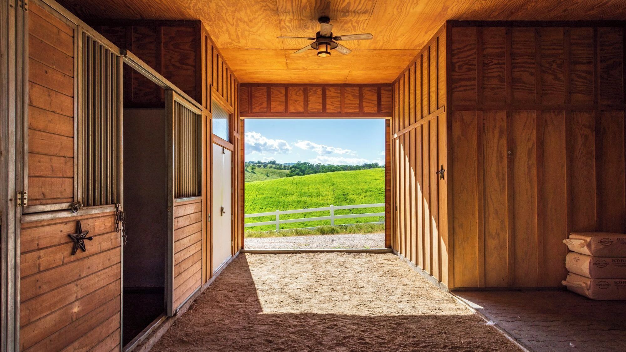 A barn with a dirt floor leading to a green field.