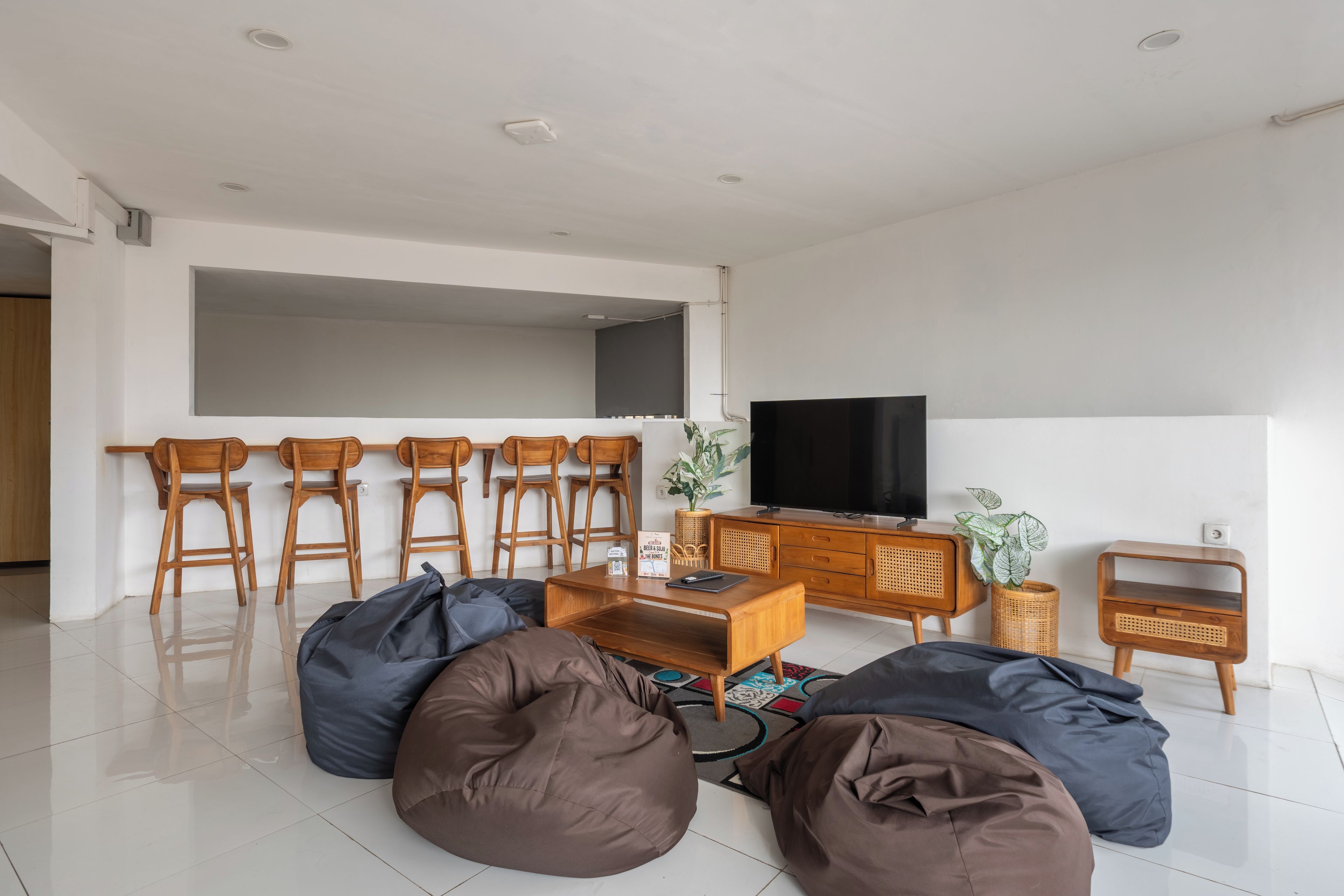 Een moderne woonkamer met een flatscreen televisie, houten stoelen, een bijzettafeltje en zitzakken.