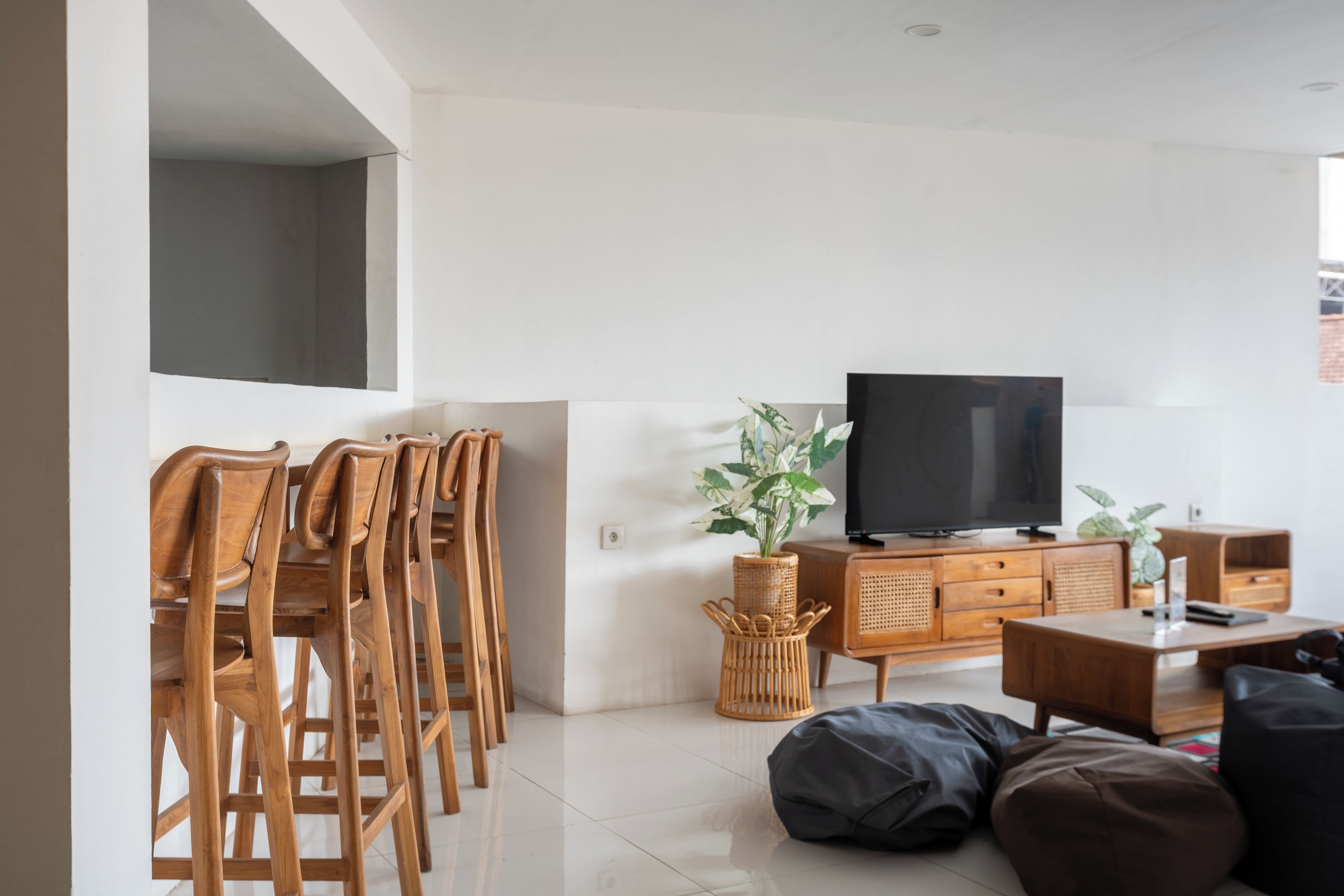 A modern living room with a flat-screen TV, wooden chairs, a sofa, and a wicker side table.
