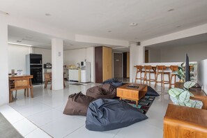 A spacious living area with a dining table, chairs, bean bags, and a kitchen in the background. - New Hostel Braga (Bandung)