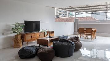 Een moderne woonkamer met een flatscreen televisie, houten meubels en een balkon met uitzicht op gebouwen.