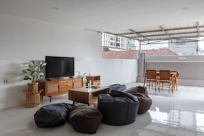 A modern living room with a flat-screen TV, wooden furniture, and a balcony with a view of buildings. - New Hostel Braga (Bandung)