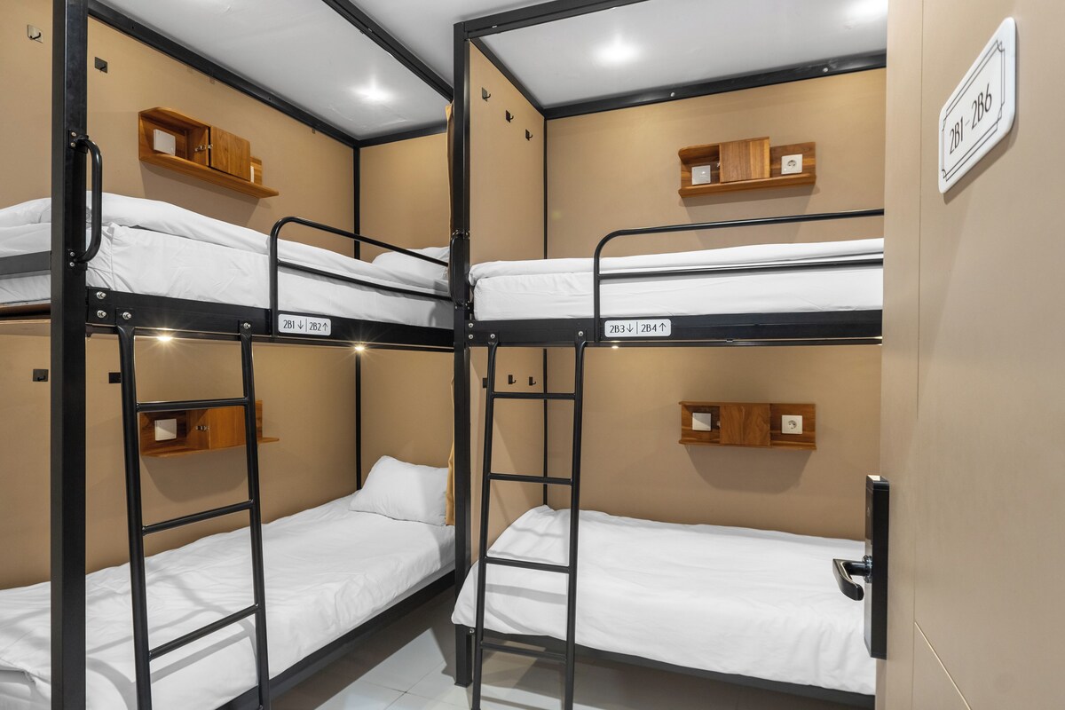 A bunk bed room with wooden headboards and a white wall sign indicating room numbers.