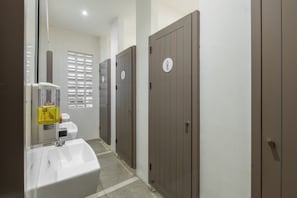 A bathroom with a sink, toilet, and three doors, each with a gender symbol.