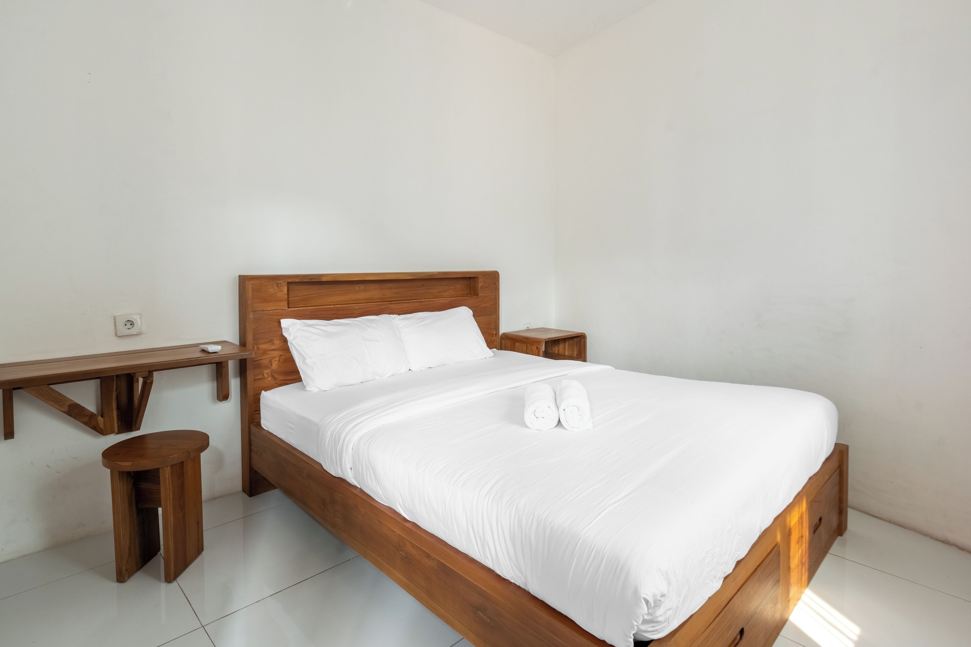A single bed with a wooden frame and white bedding, flanked by wooden nightstands and a small wooden table.
