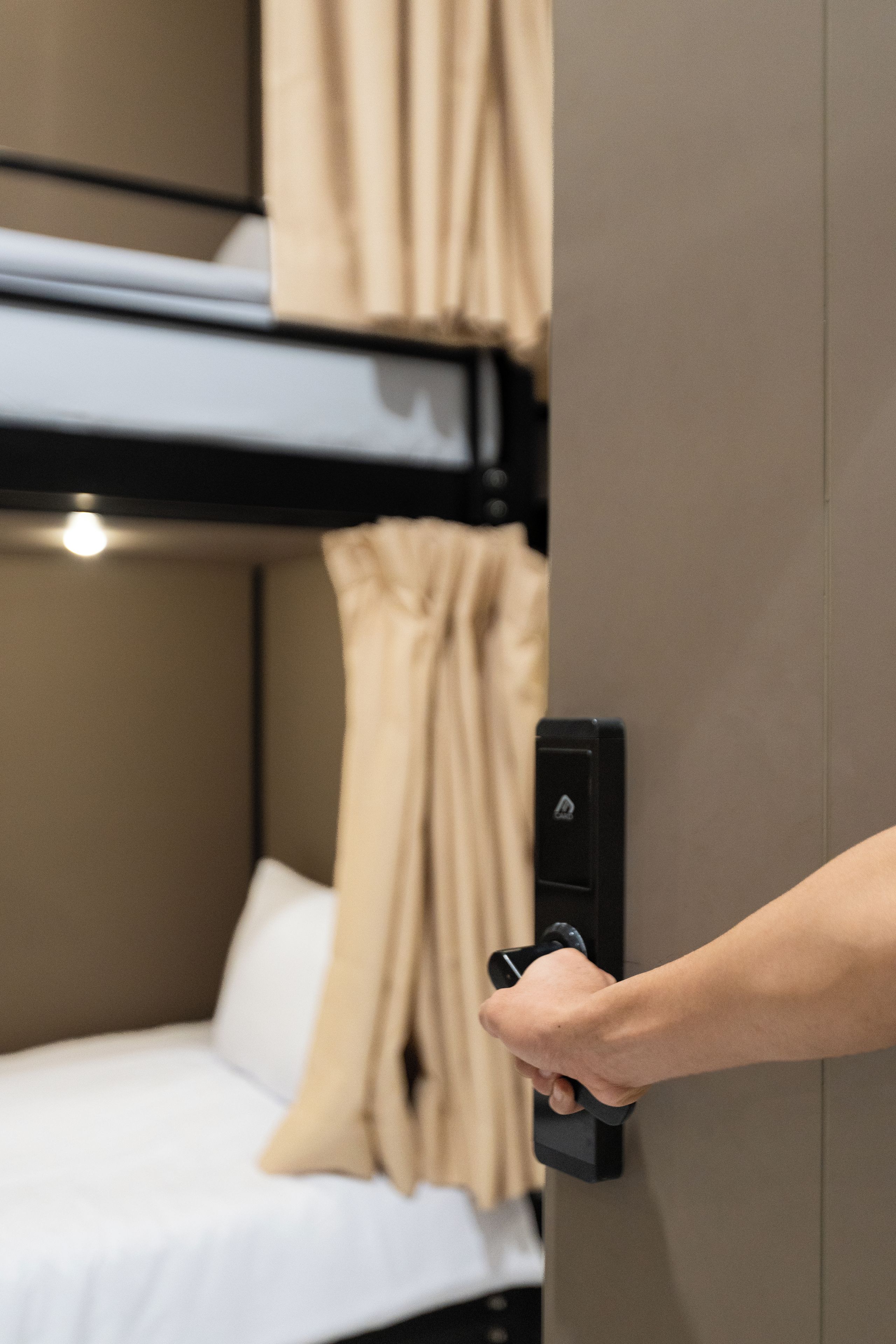 A hand operating a door handle in a room with a bunk bed and a white mattress.