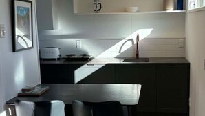 A modern kitchen with a dining area, featuring a wooden table and chairs, a coffee machine, and a view of the outdoors. - Contempory Hillside studio in Cashmere (Christchurch)
