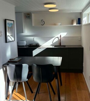Eine moderne Küche mit Essbereich, ausgestattet mit einem Holztisch und Stühlen, einer Kaffeemaschine und Blick ins Freie.