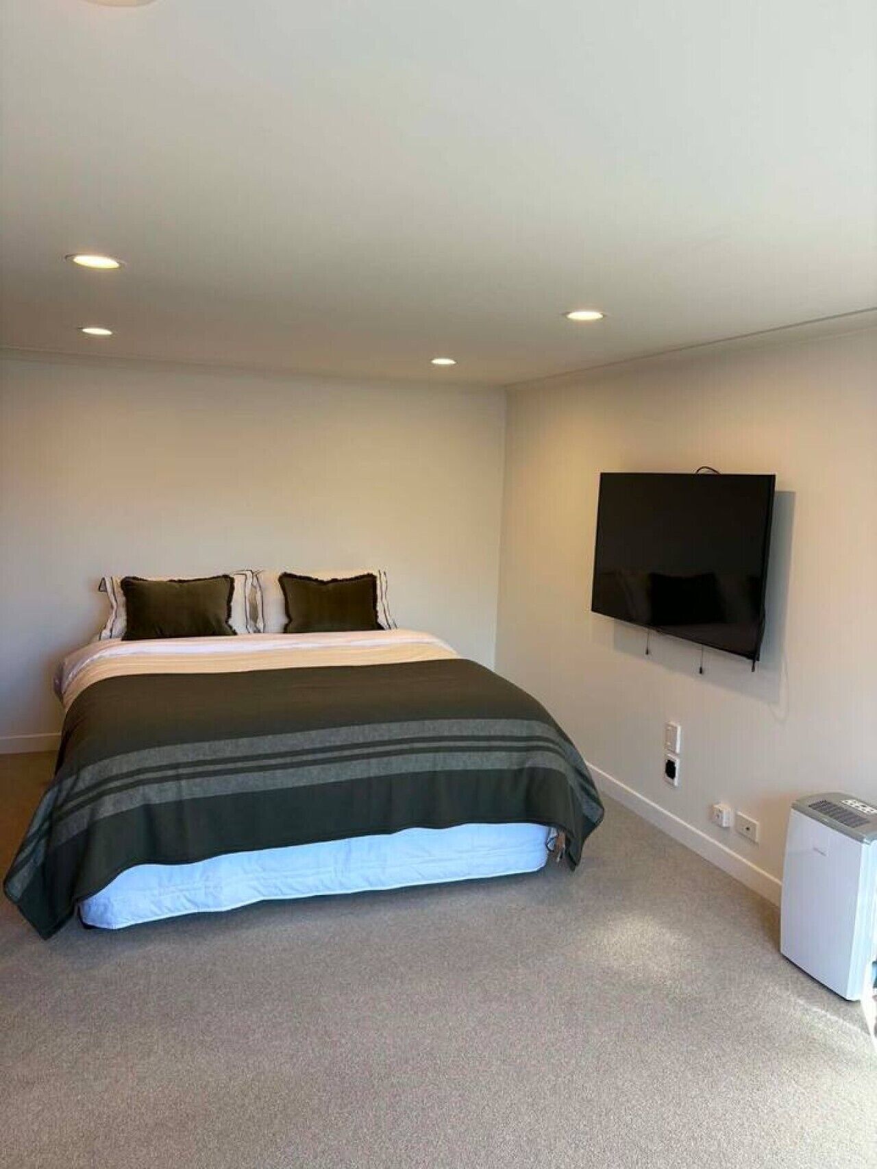 A bedroom with a bed, a television mounted on the wall, and a small white appliance on the floor.