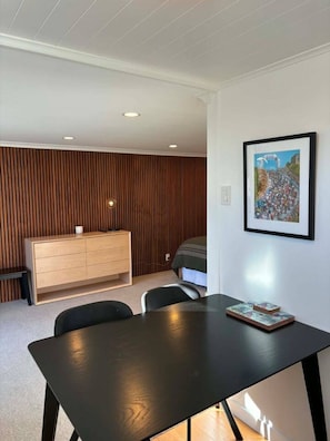 Ein modernes Zimmer mit einer Holzwand, einem schwarzen Esstisch, einer kleinen Kommode und einem gerahmten Bild an der Wand.