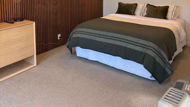 A bedroom with a bed, bedside table, and a wall-mounted heater. - Contempory Hillside studio in Cashmere (Christchurch)