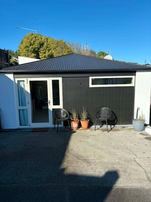 A building with a dark exterior, a sliding glass door entrance, and two chairs outside. - Contempory Hillside studio in Cashmere (Christchurch)