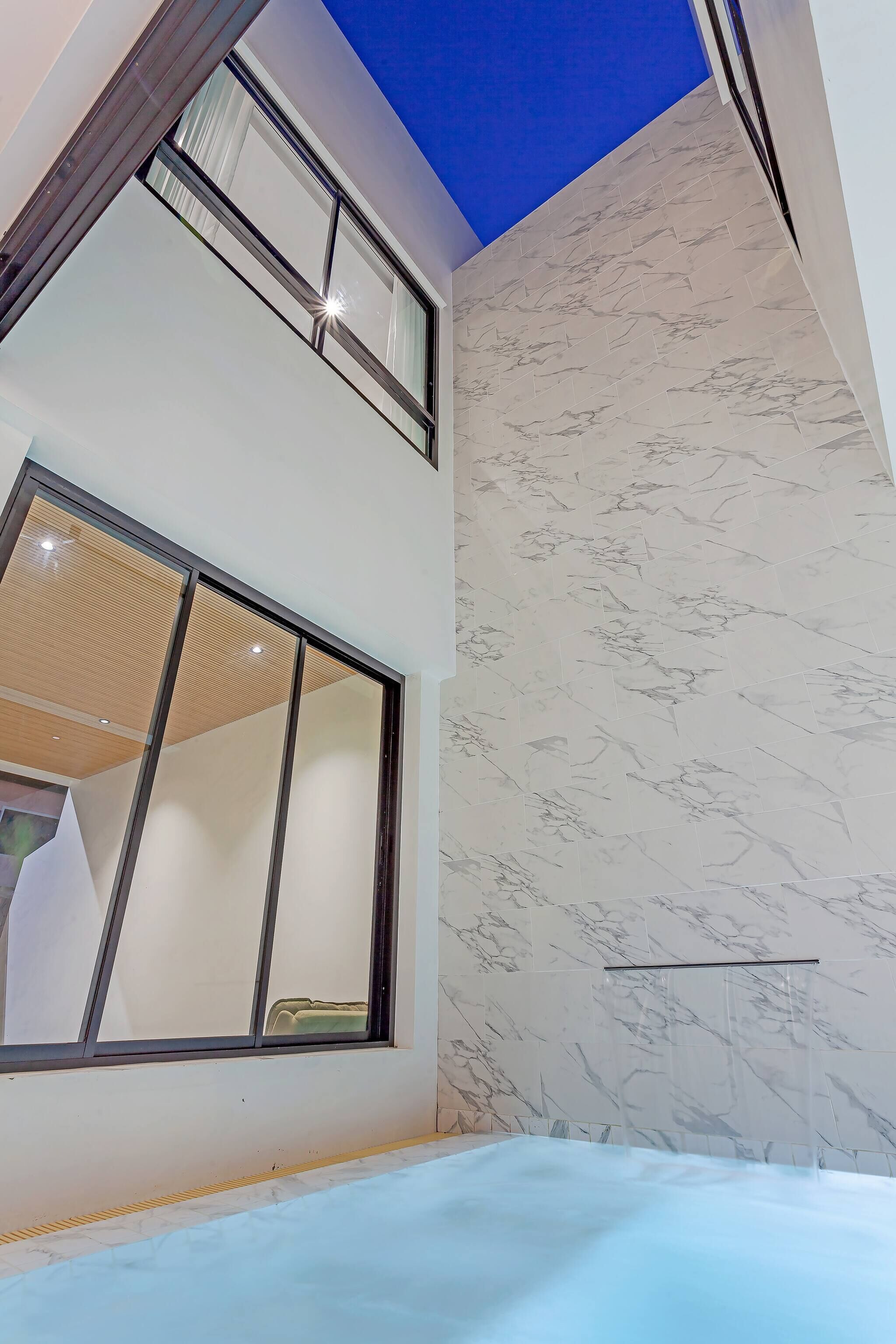 Un interior moderno con techo alto, un ventanal grande y una pared de mármol.
