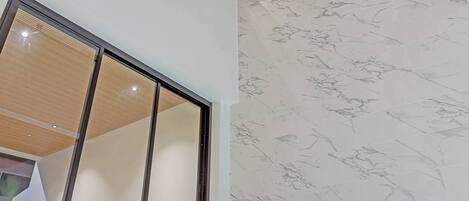Un interior moderno con techo alto, un ventanal grande y una pared de mármol.