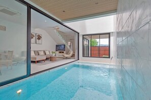 A modern indoor swimming pool with a glass wall, a sofa, and a television. - Modern Pool Villa Near Bangtoa Beach 5 Mins (Choeng Thale)