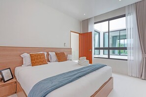 A modern hotel room with a large bed, a wooden headboard, and a view of the outdoors through a large window. - Modern Pool Villa Near Bangtoa Beach 5 Mins (Choeng Thale)