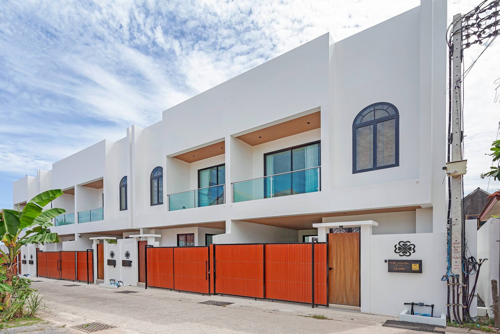 A modern multi-story residential building with balconies, a gated entrance, and a clear sky.