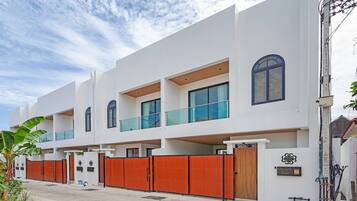 A modern multi-story residential building with balconies, a gated entrance, and a clear sky.