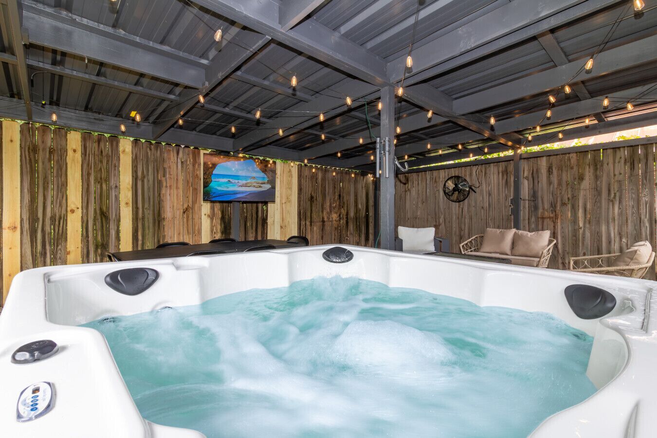 A hot tub with a wooden backdrop and a television screen displaying a beach scene.