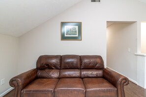 A brown leather sofa in a room with white walls and a framed picture above it. - Plaza on Peacock Ave (Columbus)