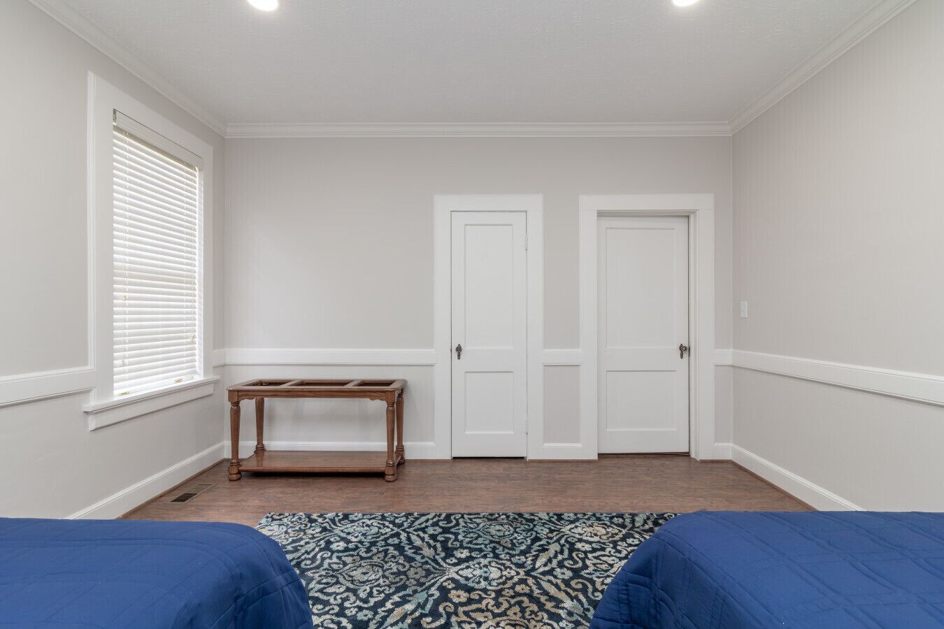 A room with two white doors, a wooden table, and a patterned rug.