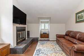 A living room with a fireplace, a brown leather sofa, and a patterned rug. - Plaza on Peacock Ave (Columbus)