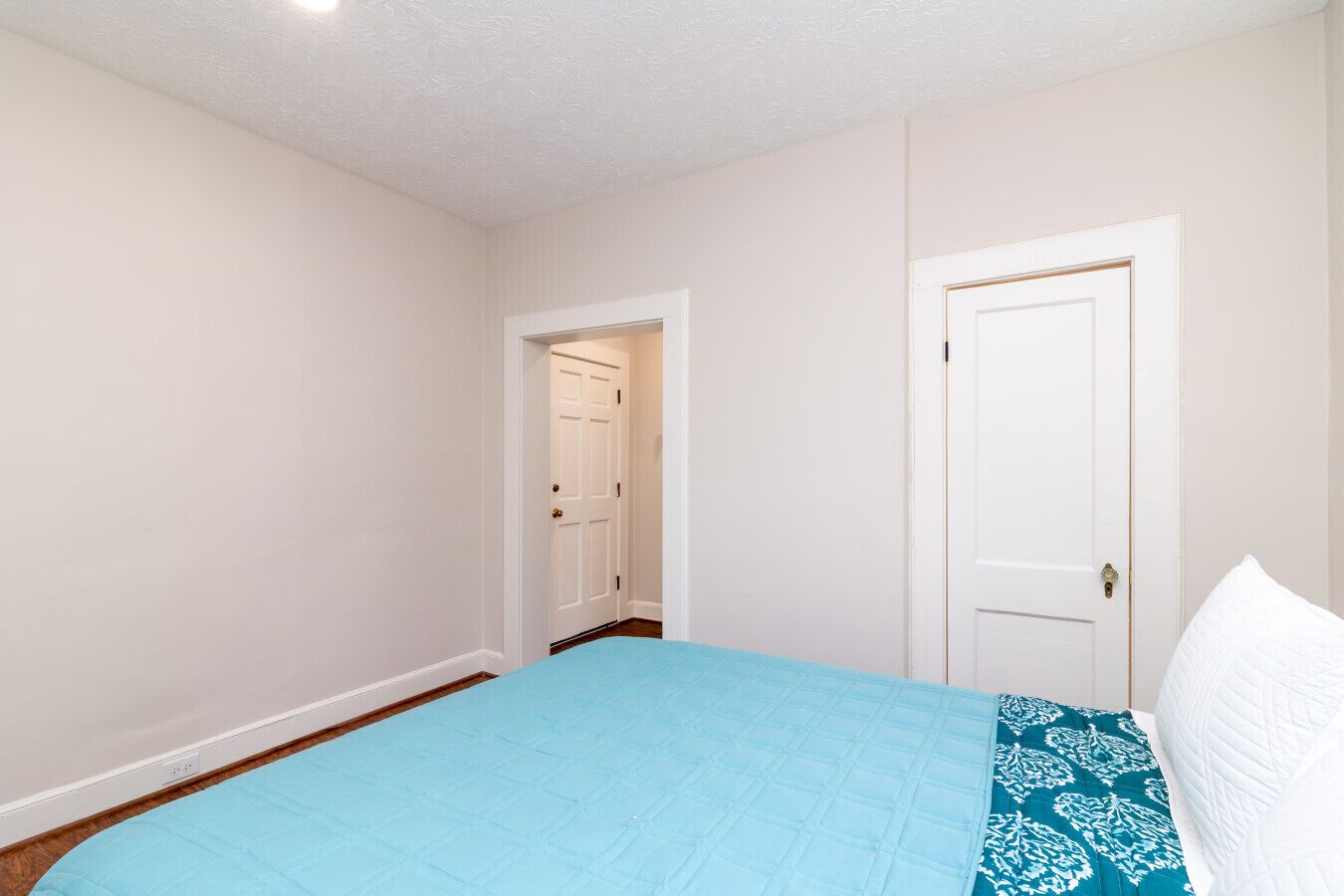 A bedroom with a single bed, a white door, and a hallway leading to another room.