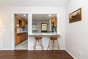A kitchen with wooden cabinets, a white countertop, and two bar stools. - Plaza on Peacock Ave (Columbus)