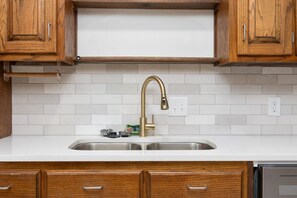 A kitchen with wooden cabinets, a stainless steel sink, and a gold faucet. - Plaza on Peacock Ave (Columbus)