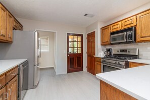 A kitchen with wooden cabinets, a stainless steel refrigerator, a microwave, a stove, and a dishwasher. - Plaza on Peacock Ave (Columbus)