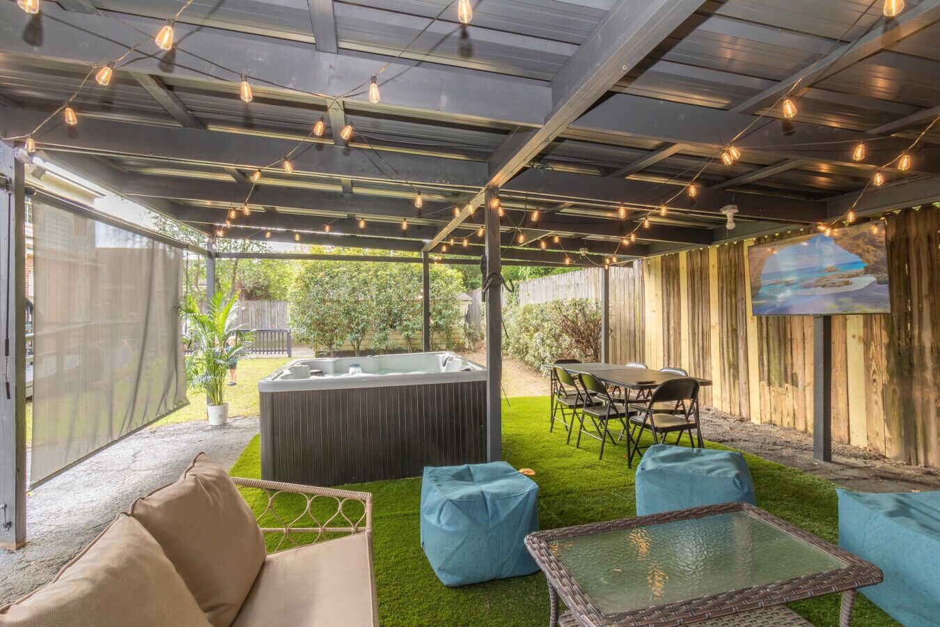An outdoor patio with a hot tub, seating area, and string lights.