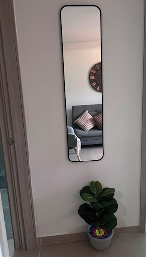 A wall-mounted mirror with a reflection of a room containing a grey sofa and a round wall clock. - 29.6 Stunning 29th-Floor Apartment | Pool, Gym, and Parking (Sabaneta)