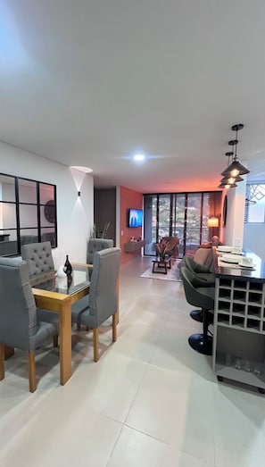 A modern living room with a dining area, a flat-screen TV, and a large window offering a view. - 29.6 Stunning 29th-Floor Apartment | Pool, Gym, and Parking (Sabaneta)