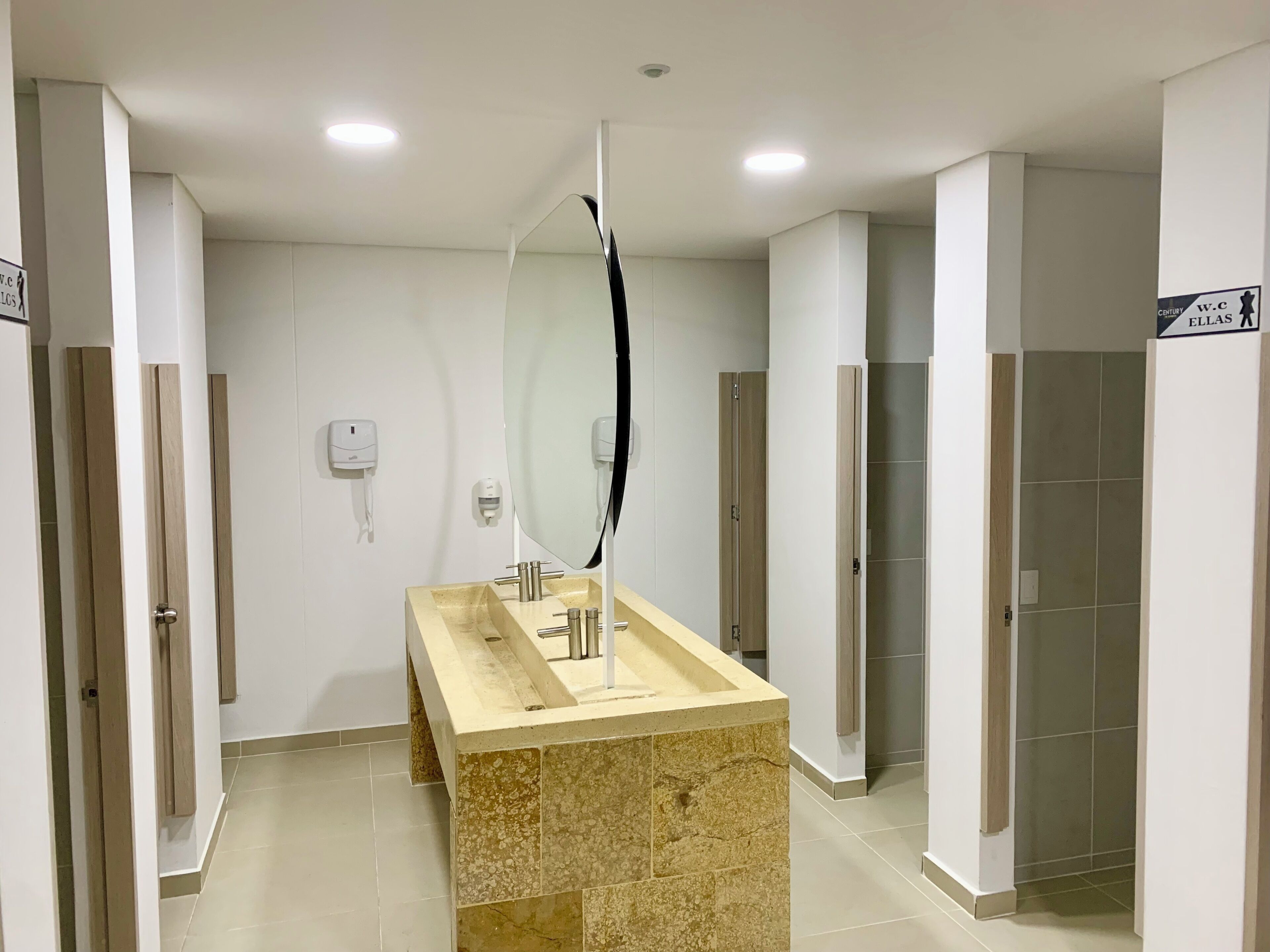 A modern bathroom with a beige marble sink, a large mirror, and a hand dryer.