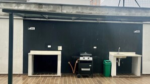 Uma área externa coberta com churrasqueira, pia e lixeira.