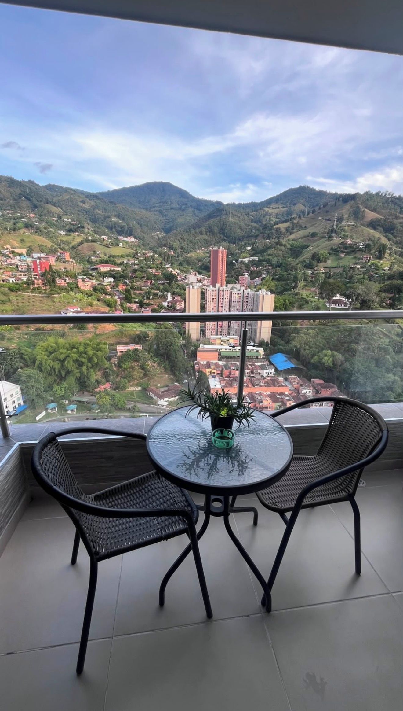 Un balcon avec deux chaises et une table, donnant sur un paysage montagneux parsemé de bâtiments.