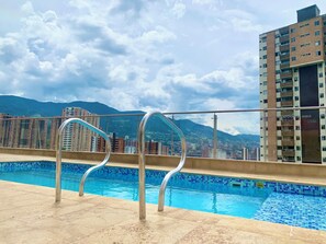 Ein Pool auf dem Dach mit Metallgeländern, einer gefliesten Kante und einer Stadtansicht mit Bergen im Hintergrund.