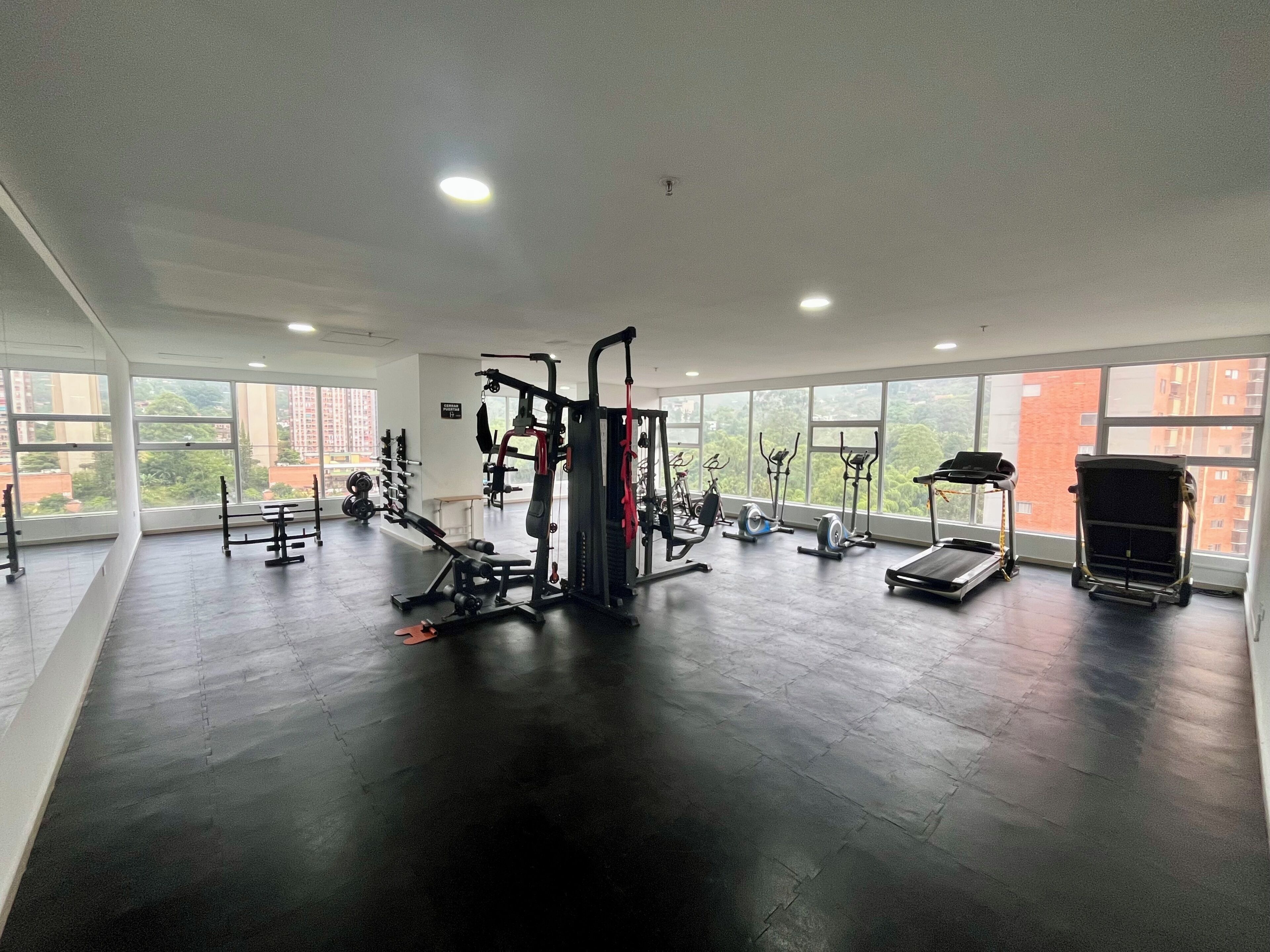 A gym with various exercise equipment, large windows, and a high ceiling.