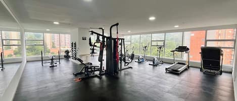 A gym with various exercise equipment, large windows, and a high ceiling.
