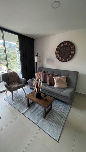 Ein modernes Wohnzimmer mit einem grauen Sofa, zwei Sesseln, einem Holztisch und einer großen Wanduhr.