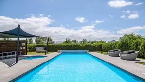 Une piscine rectangulaire à l’eau d’un bleu limpide, entourée d’une terrasse dallée. On y trouve des chaises longues et un espace salon abrité sur la terrasse.